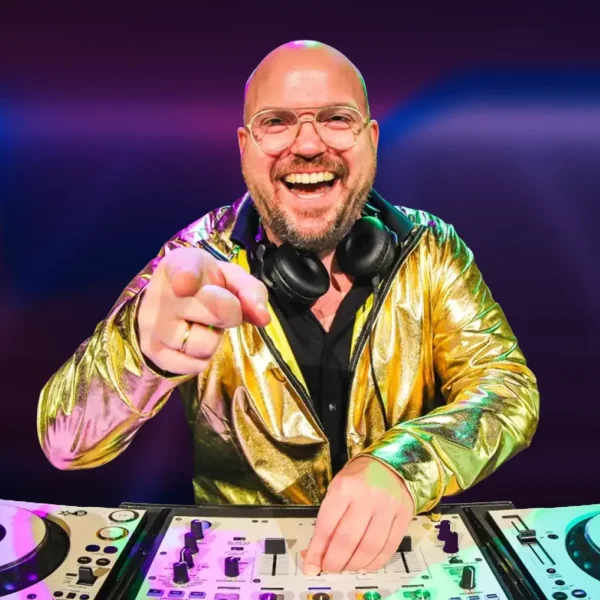 Afbeelding van DJ Royaal (Dimitri Visch) Royaal Artists achter de draaitafels tijdens een bruisend event of cluboptreden. Hij staat gefocust bij zijn apparatuur, omringd door sfeervolle verlichting en een dansend publiek op de achtergrond